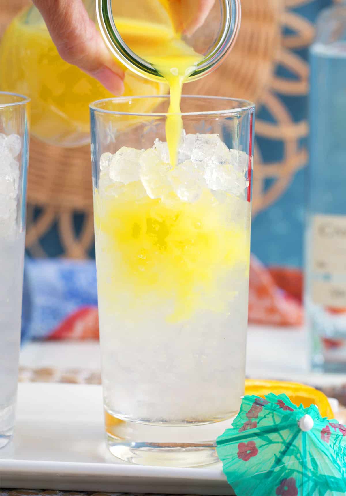 orange juice is being poured into a collins glass with ice to make a tequila sunrise