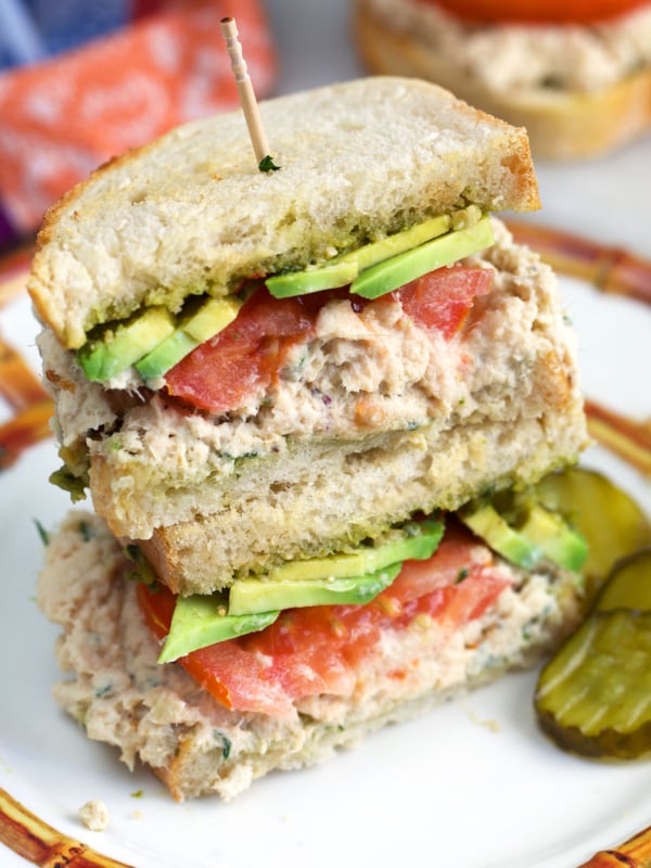 Tunacado sandwich on sourdough bread on a plate with pickles on the side.