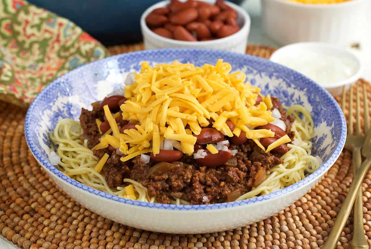 Cincinnati Chili in a blue and white bowl topped with onions, cheese and beans.
