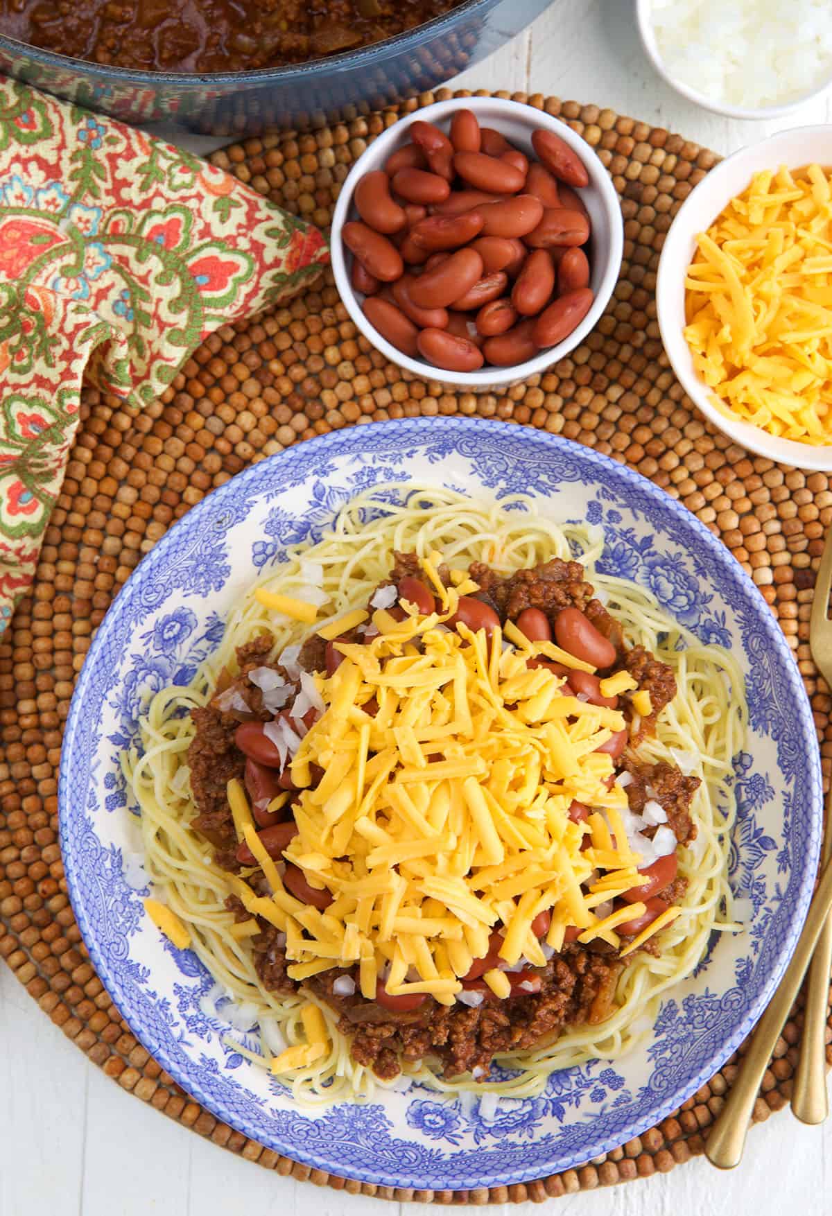 Cincinnati Chili topped with cheese and bowls of kidney beans and cheese on the side.