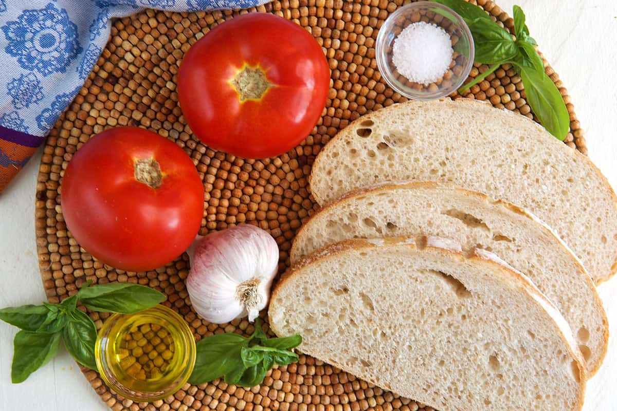 ingredients for pan con tomate, bread slices, two tomatoes, basil, olive oil, garlic and salt.