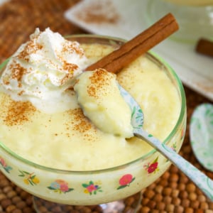 tapioca pudding in a small compote dish with whipped cream and a cinnamon stick on top.
