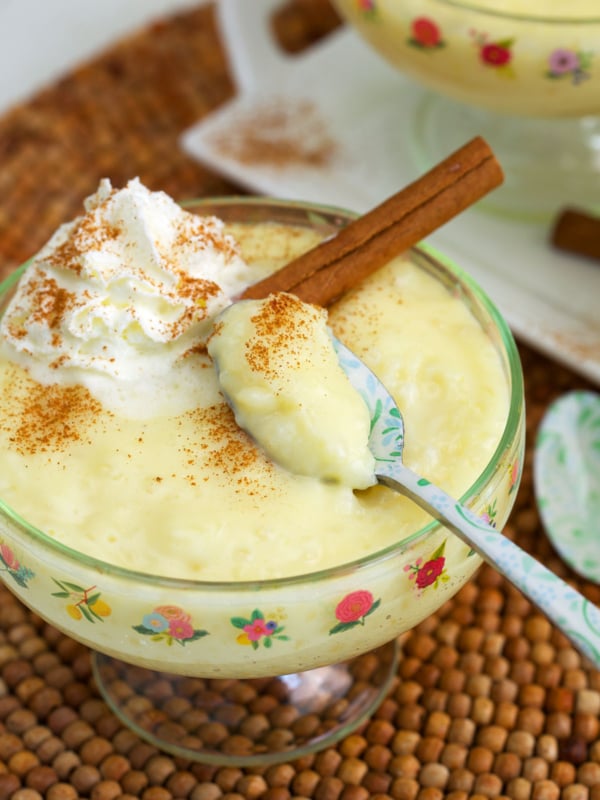 tapioca pudding in a small compote dish with whipped cream and a cinnamon stick on top.