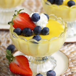 Vanilla custard in a glass dessert coupe topped with berries and whipped cream