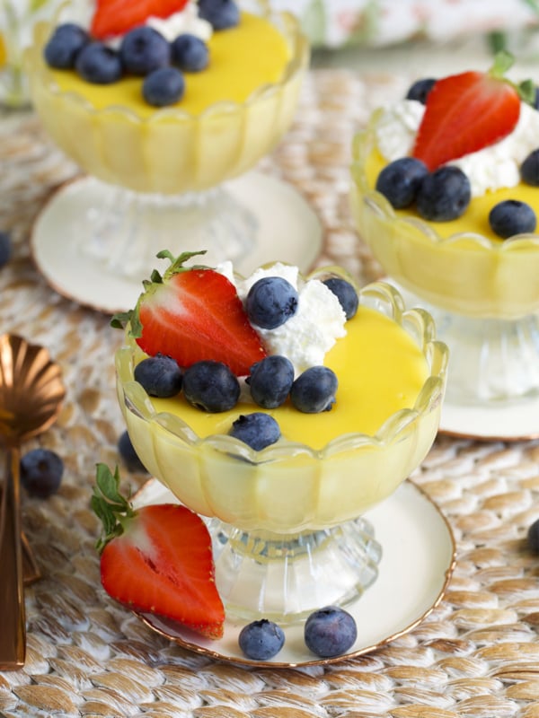 vanilla custard in glass dishes ready to be served topped with berries and whipped cream.