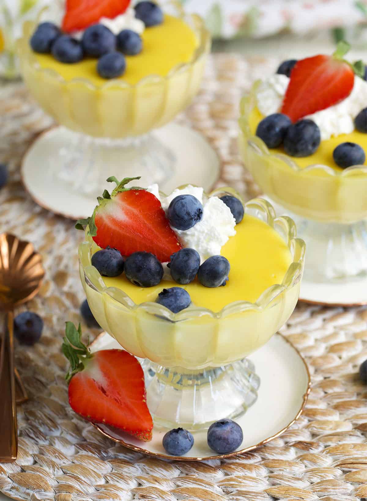 vanilla custard in glass dishes ready to be served topped with berries and whipped cream.