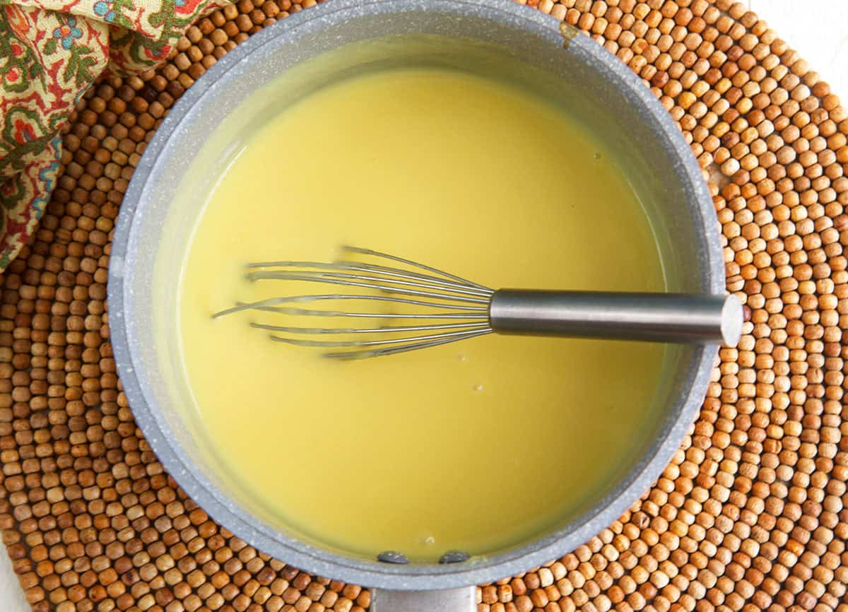 vanilla custard recipe being cooked in a saucepan with a whisk