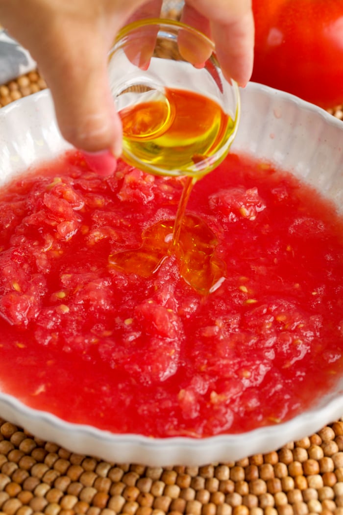 olive oil being added to grated tomato in a bowl