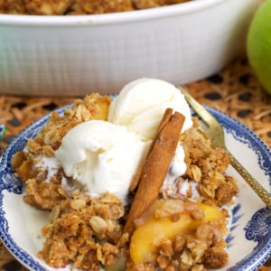apple crumble on a blue and white transfer ware plate topped with ice cream and a cinnamon stick.