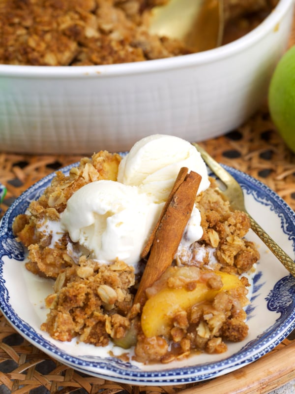 apple crumble on a blue and white transfer ware plate topped with ice cream and a cinnamon stick.