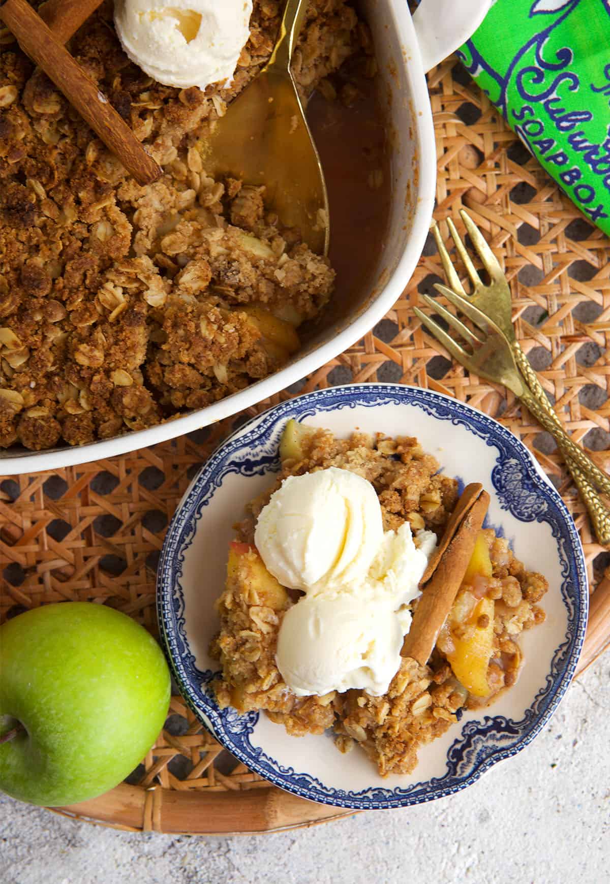 apple crumble being served on a blue and white plate from a white baking dish.