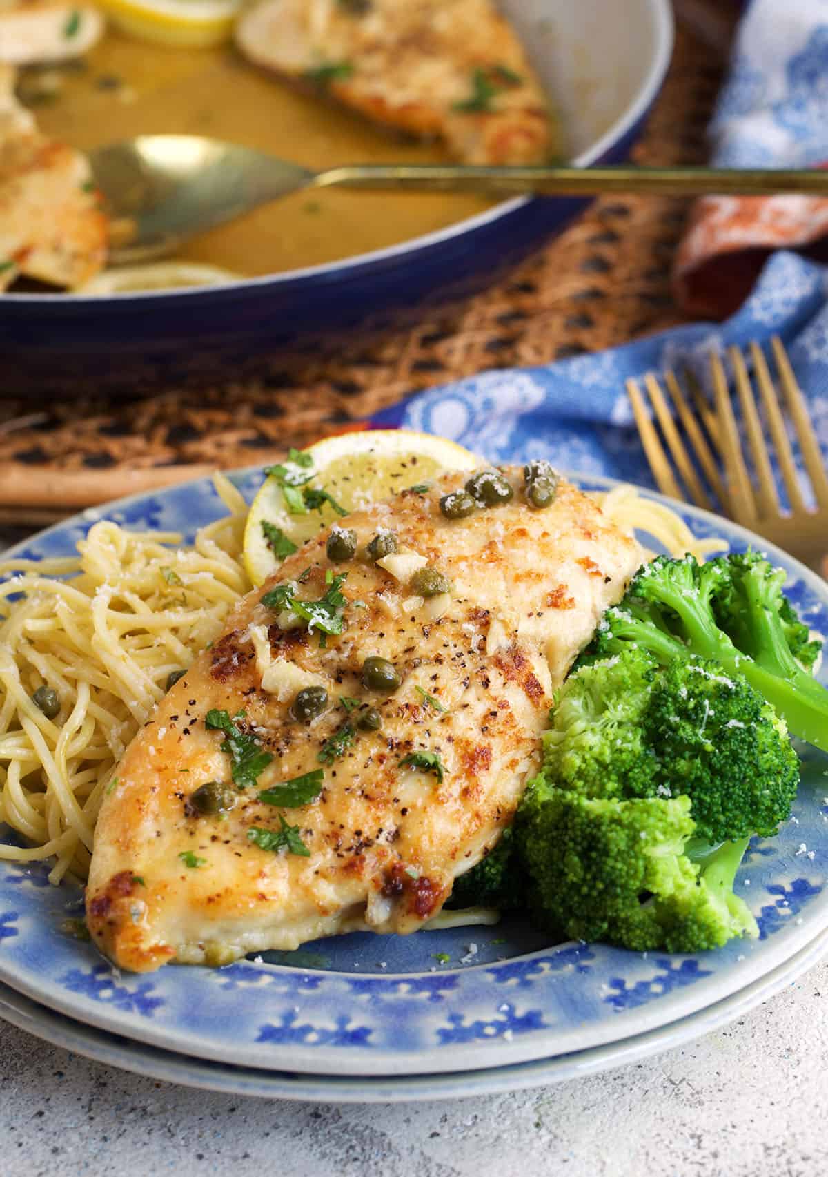 Chicken Piccata plated with pasta and broccoli on a blue plate.
