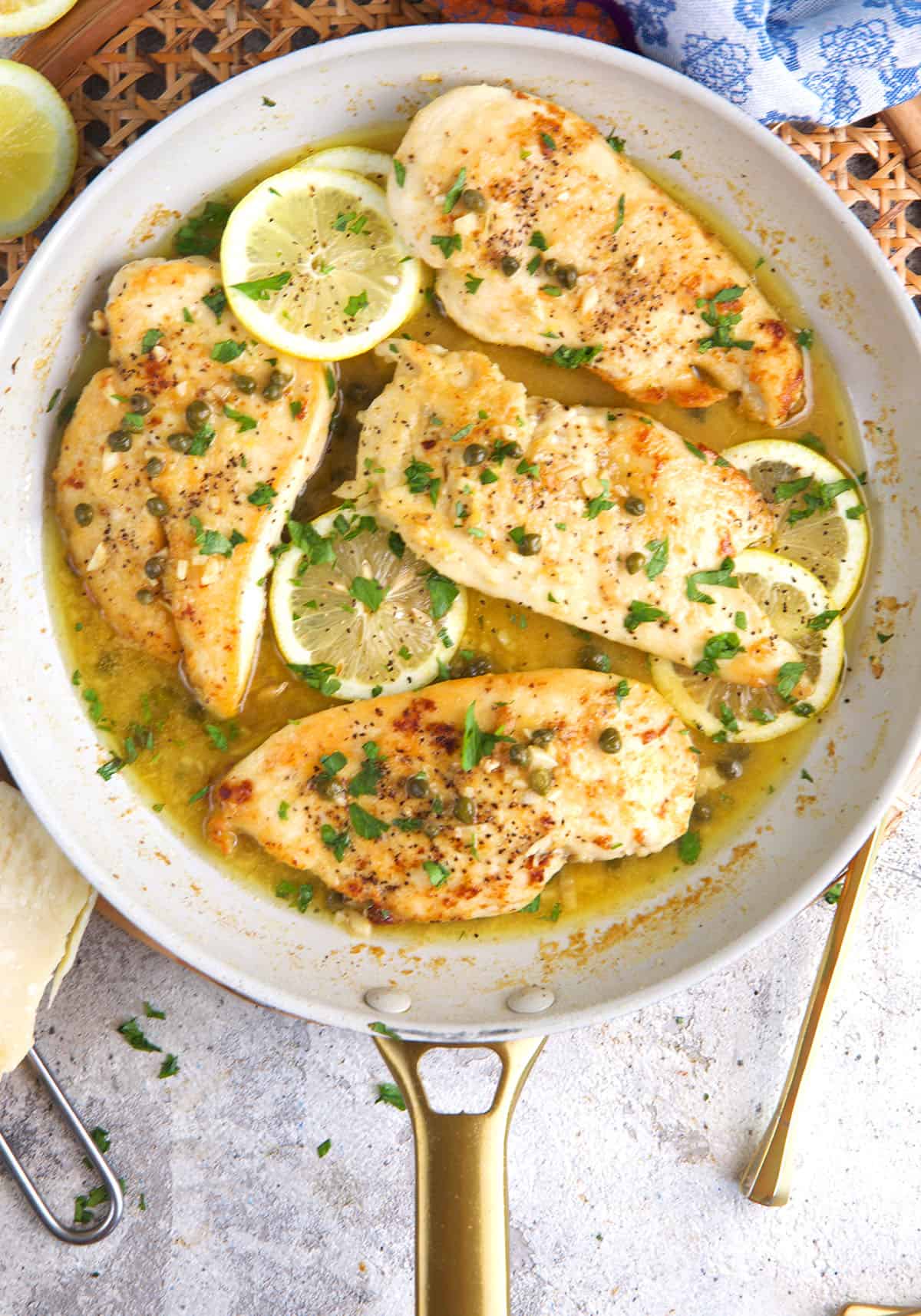 Chicken Piccata being finished in a white skillet with lemon slices.