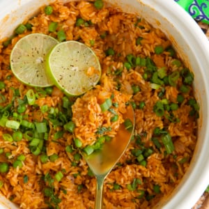 Mexican Rice in a white pot topped with lime slices and a wooden spoon