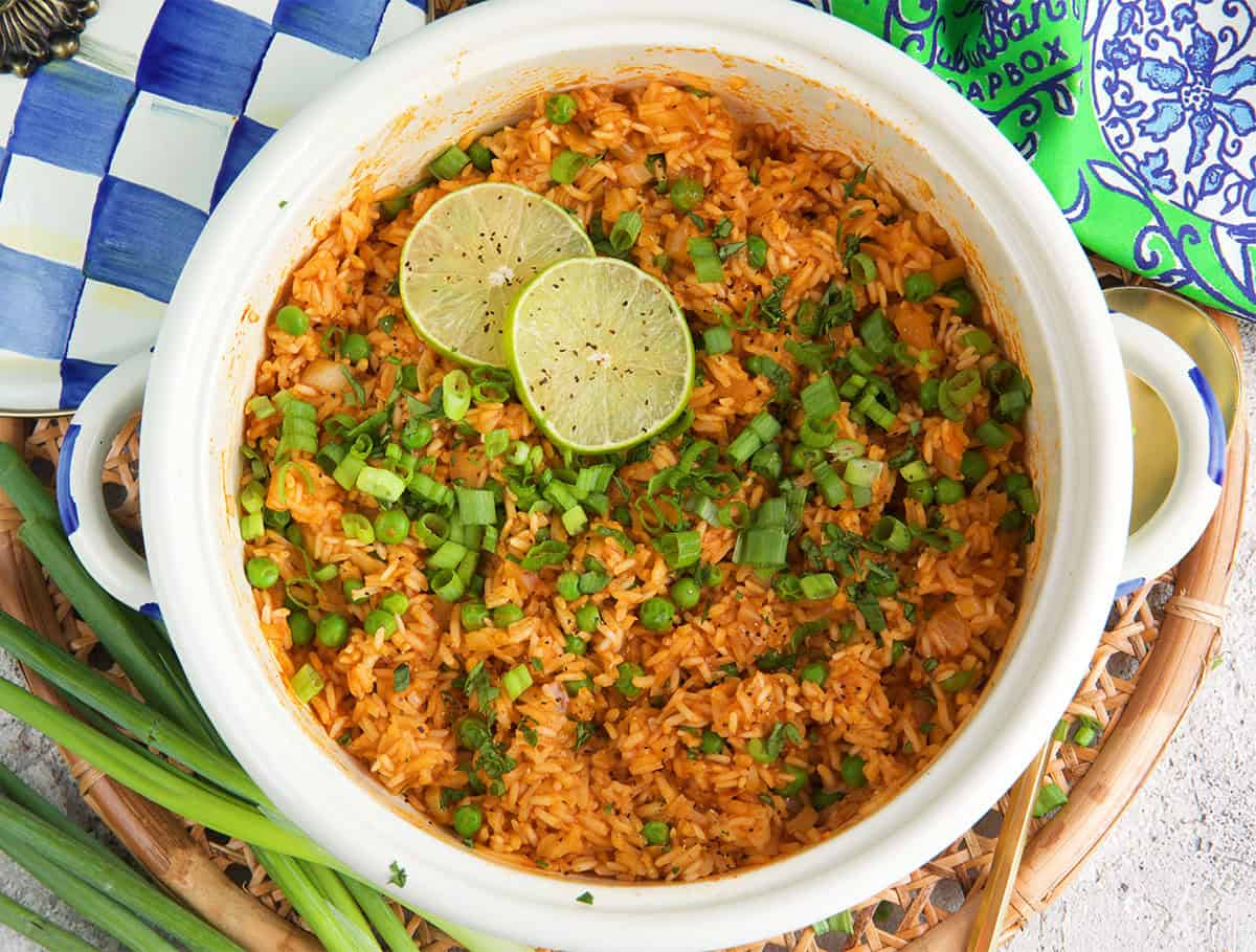 Mexican rice in a white pot with a Mckenzie Childs lid and slices of lime.
