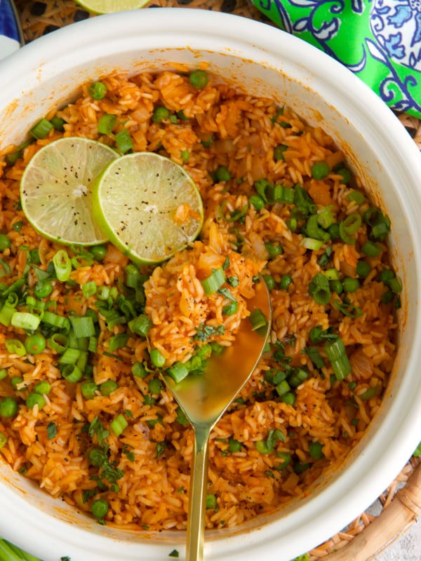 Mexican Rice in a white pot topped with lime slices and a wooden spoon