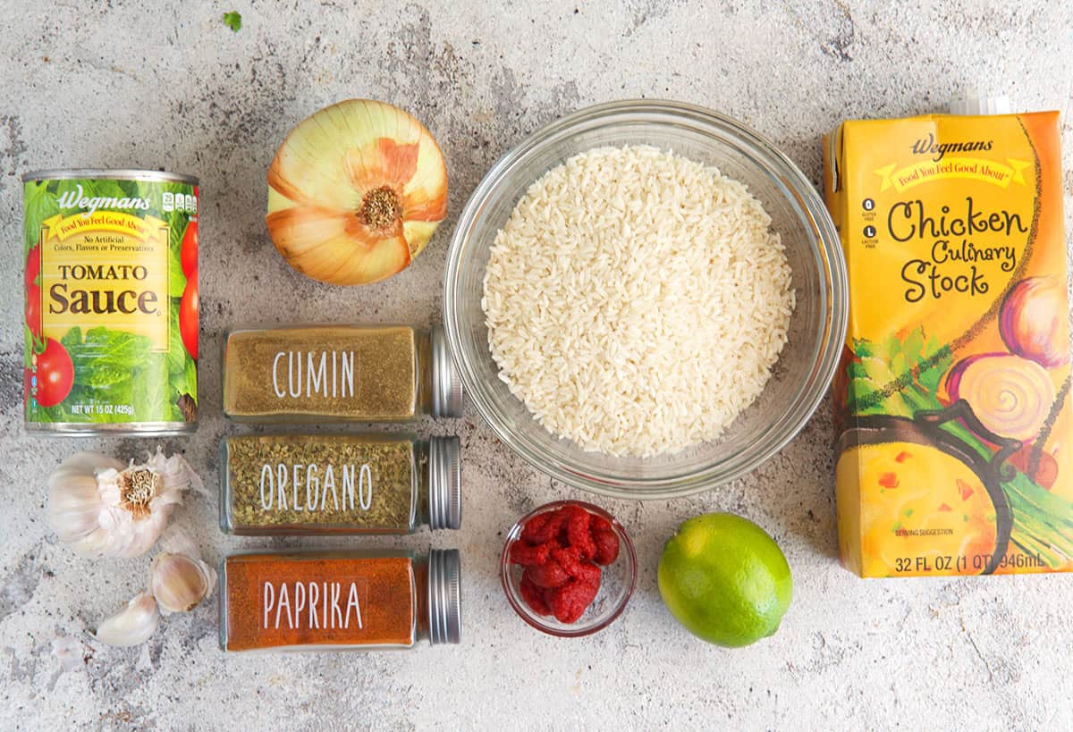 Ingredients for mexican rice, chicken stock, spices, tomatoes, rice, lime, tomato paste and garlic.