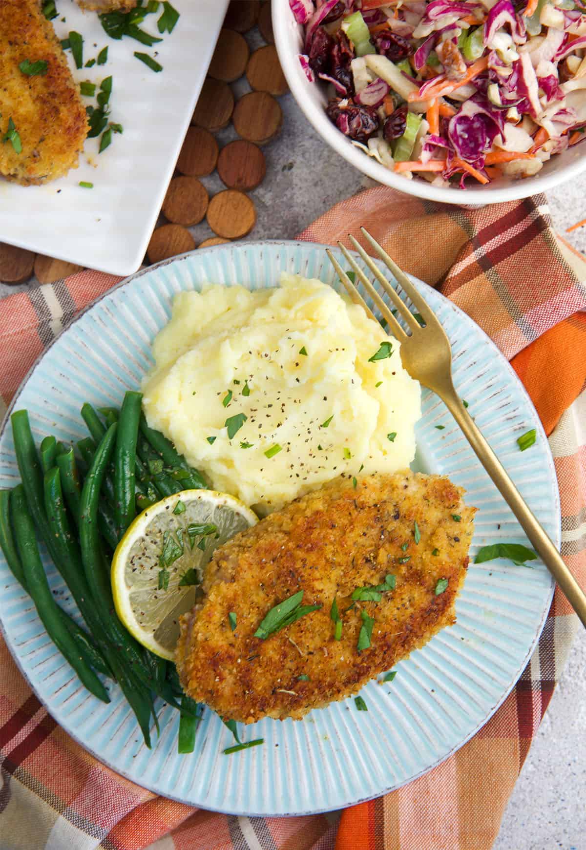 breaded pork loin chops on a plate with green beans and mashed potatoes.