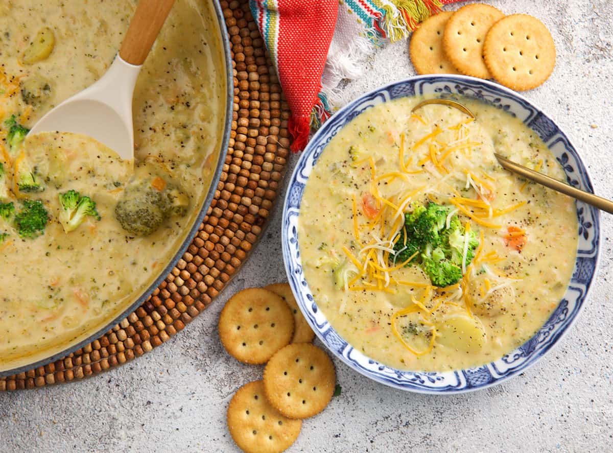 Broccoli potato soup in a blue and white bowl topped with chopped broccoli with butter crackers on the side.