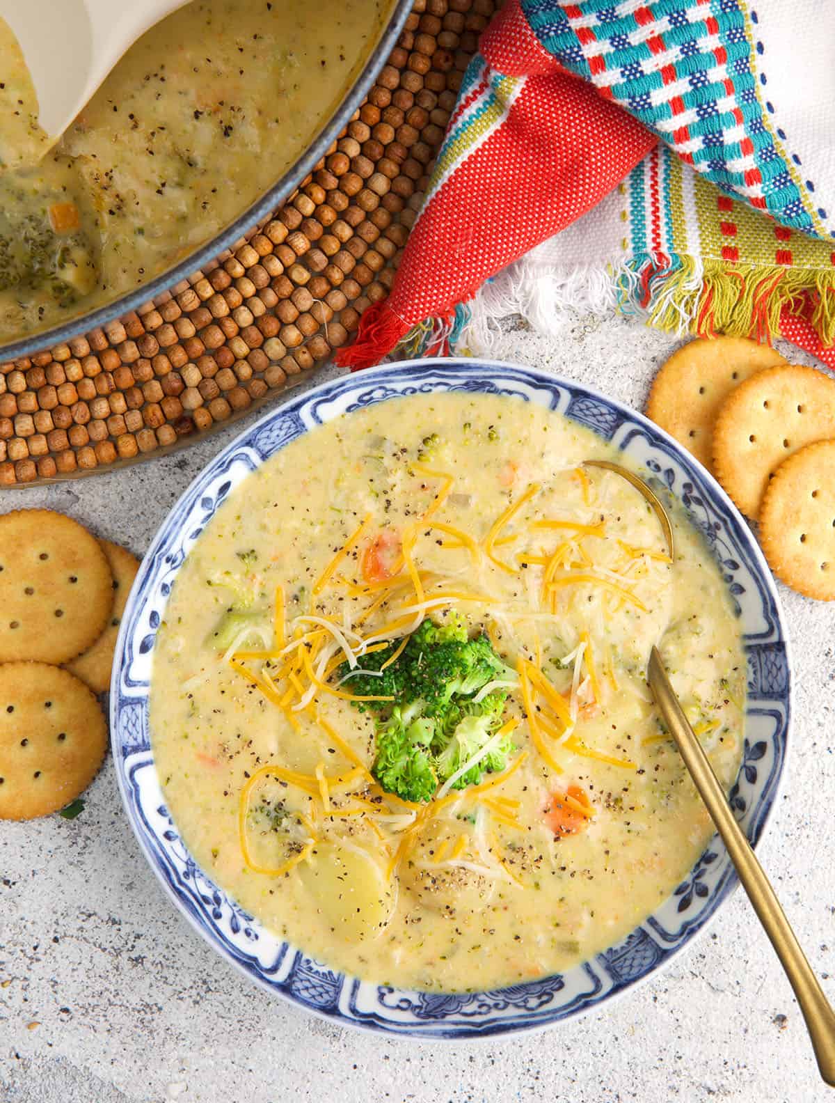 a bowl of broccoli potato soup with a gold spoon and crackers on the side.