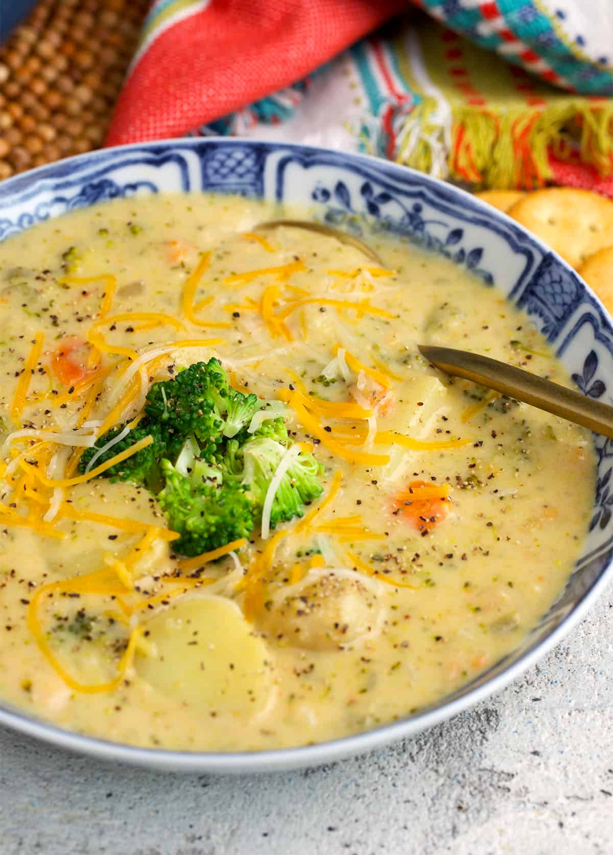 creamy broccoli potato soup topped with cheese and broccoli served in a blue and white bowl.