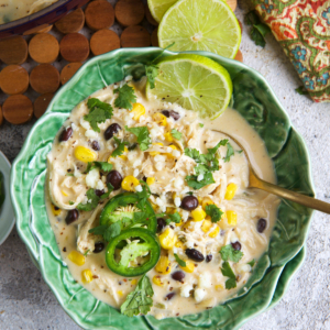 Chicken Poblano Soup in a cabbage ware bowl with limes on top.