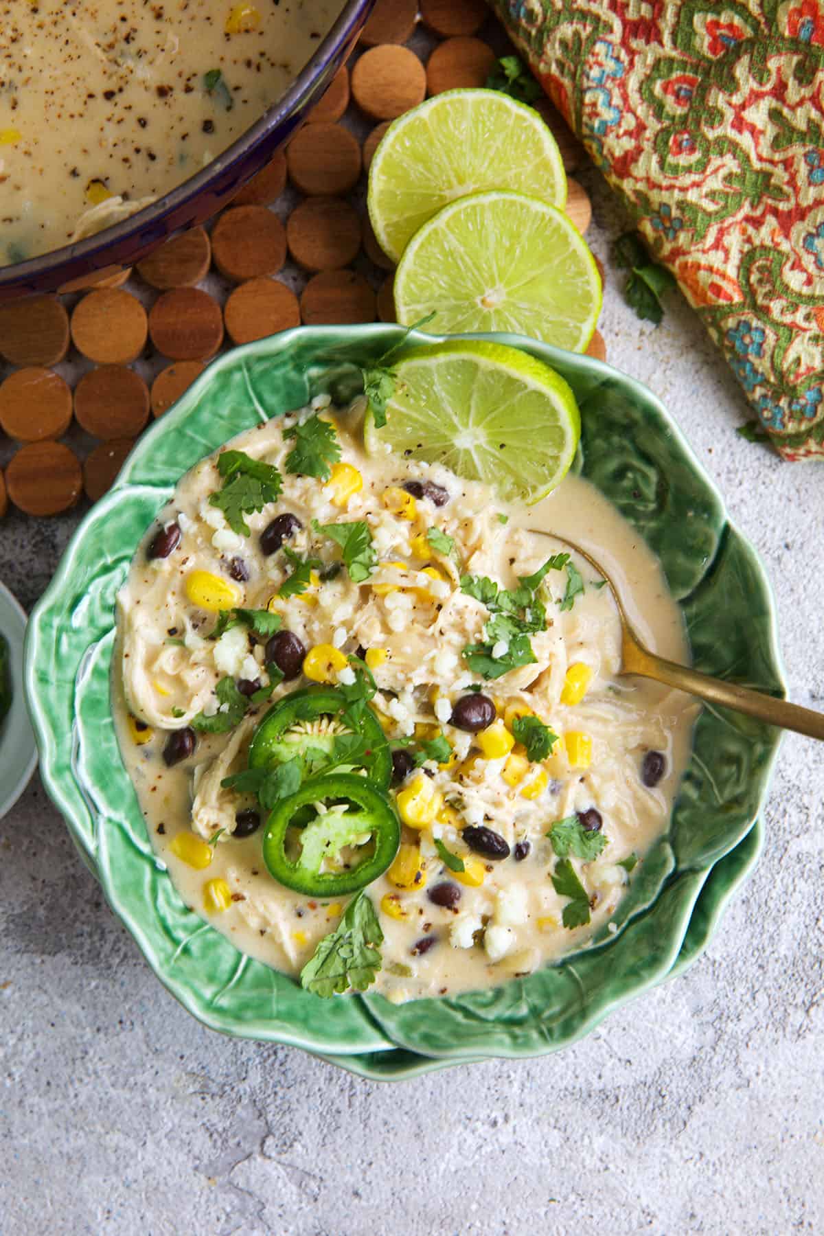 Chicken Poblano Soup in a cabbage ware bowl with limes on top.