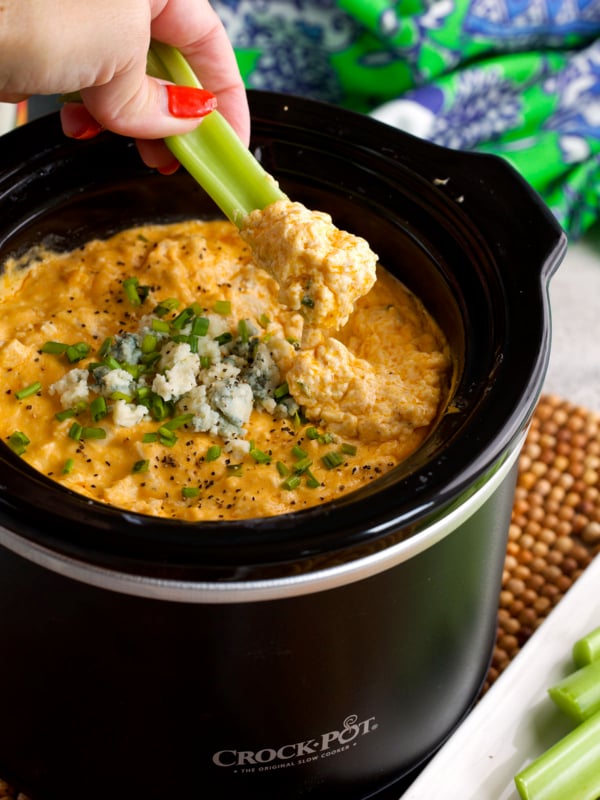 Buffalo Chicken Dip in a slow cooker with a piece of celery dipping into it.