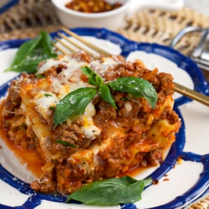 crockpot lasagna on a plate topped with basil and crushed red pepper flakes.