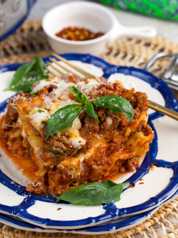crockpot lasagna on a plate topped with basil and crushed red pepper flakes.