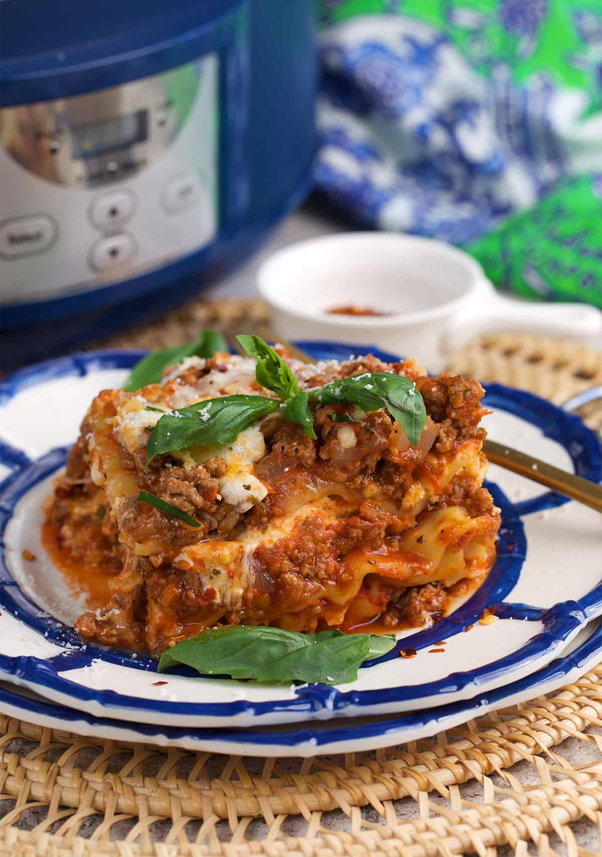 a slice of crockpot lasagna on a plate with a crockpot in the background.