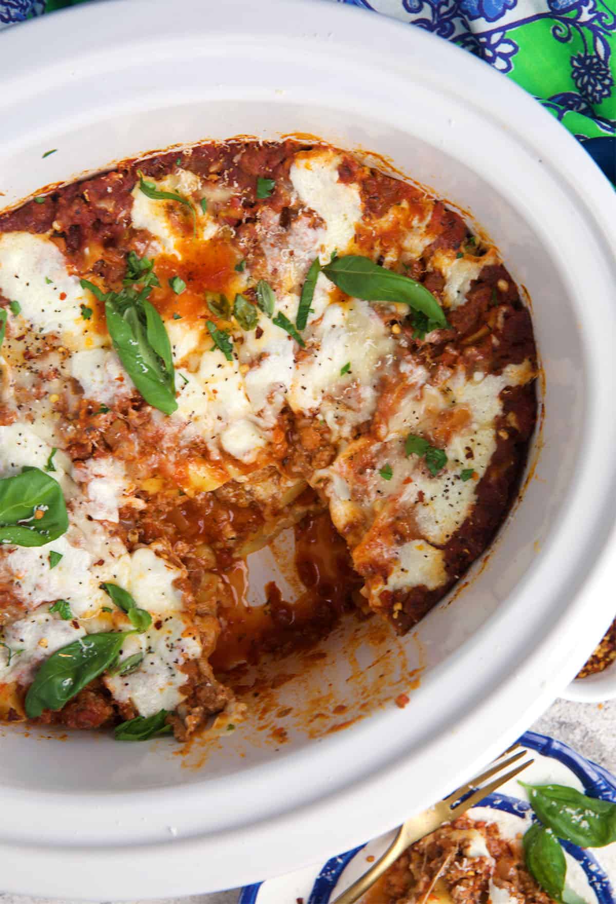 slow cooker lasagna in a crock pot with a piece cut out of it.