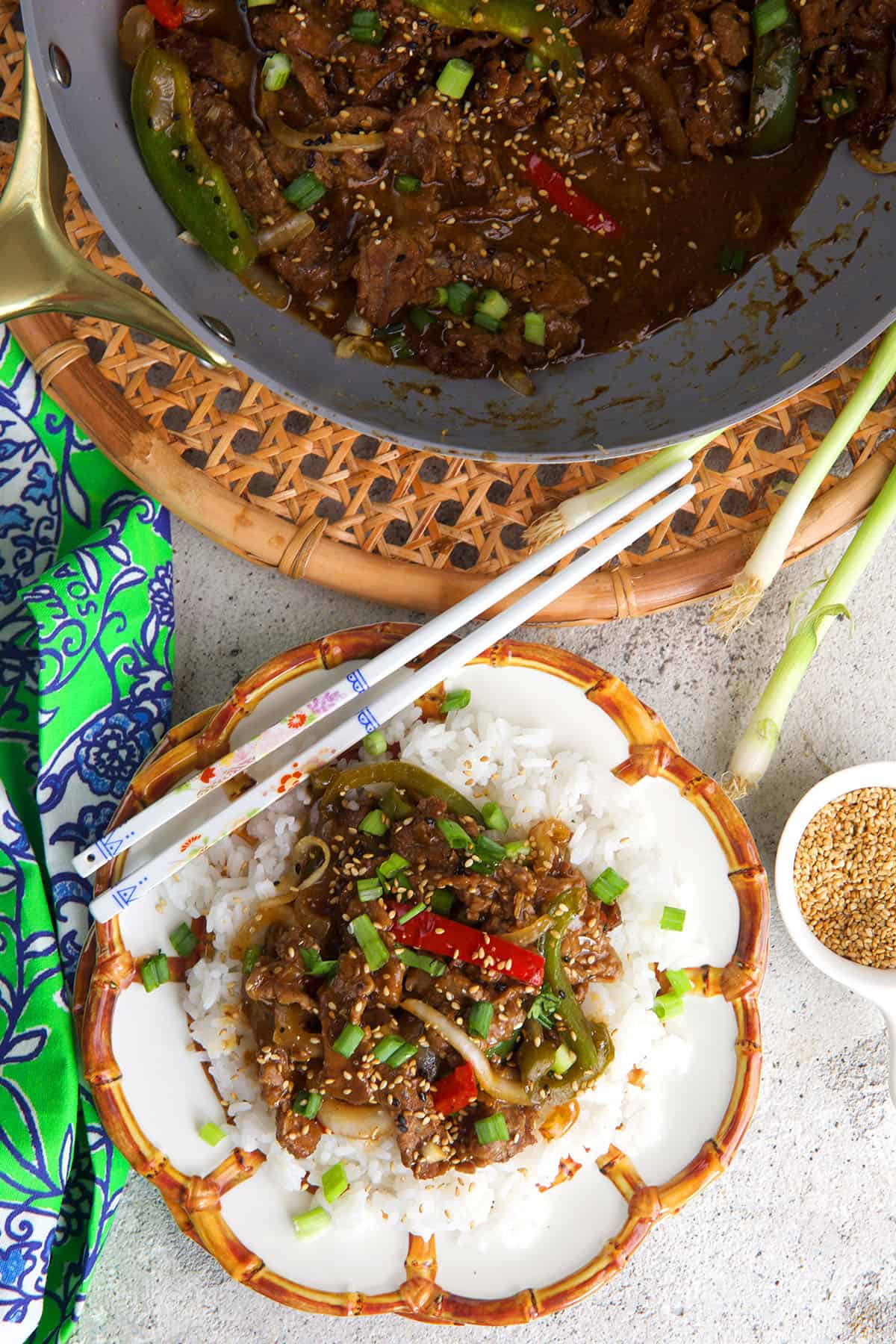 pepper steak stir fry over rice on a white and bamboo plate with white chopsticks.