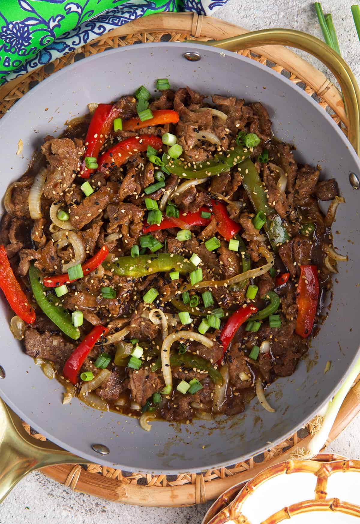 pepper steak with green peppers and red peppers with onion in a non-stick stir fry pan.