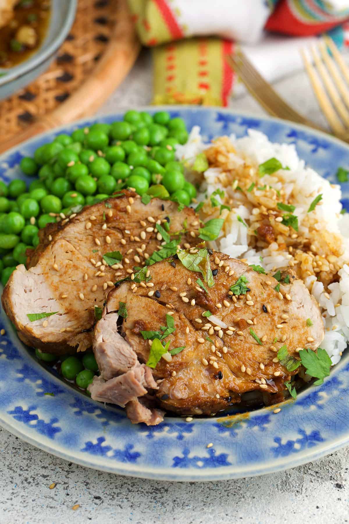 two slices of pork loin on a blue plate with peas and rice.