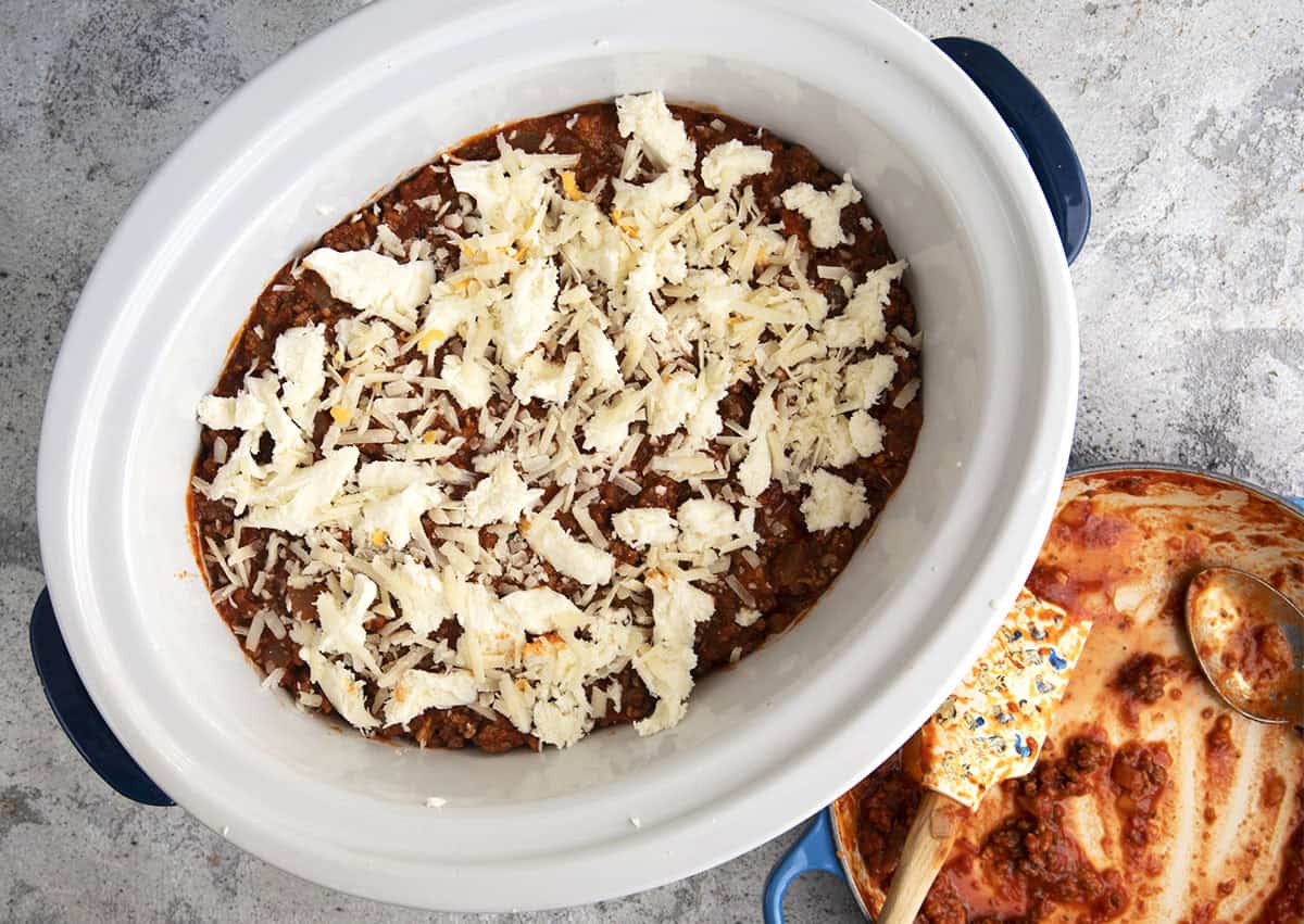 sauce and cheese being layered on the noodles in a slow cooker for crockpot lasagna