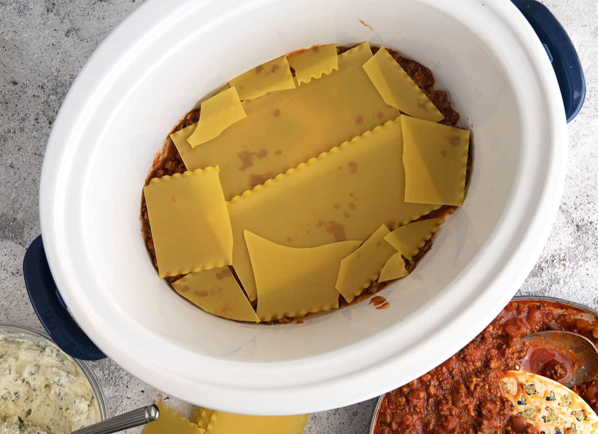 sauce and noodles being layered in the bottom of a slow cooker for crockpot lasagna